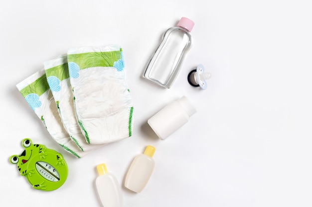 Babies goods diaper, baby powder, cream, shampoo, oil on white background with copy space. Top view or flat lay. Maternity concept