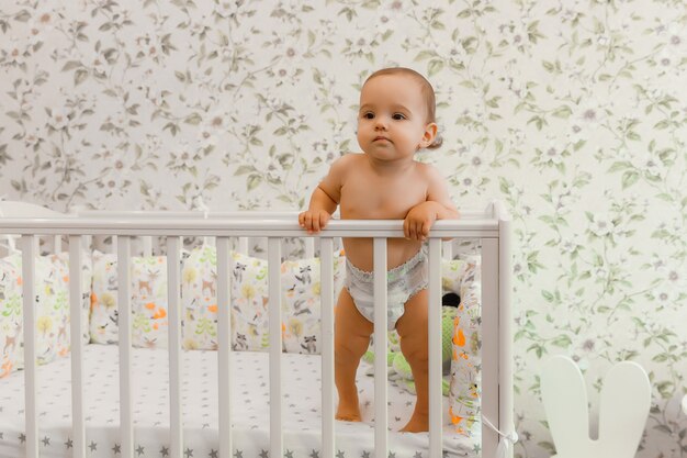 A baby of 11 months in a diaper stands in his crib child in the bed