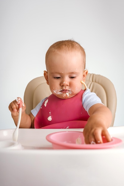 Un bambino di 12-15 mesi si siede su una sedia per mangiare e raggiunge un piatto di cibo con la mano, foto verticale