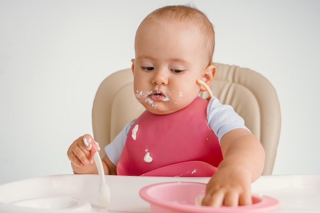 A baby 12-15 months old sits on a feeding chair and reaches into a plate of food with his hand