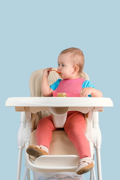 A baby of 1217 months eats vegetable puree sitting on a feeding chair