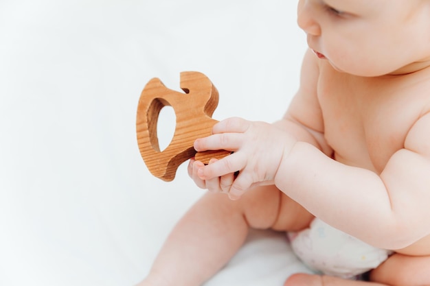 Baby 6 months old holds in his hands a wooden teething toy lying in a cradle in a children's room