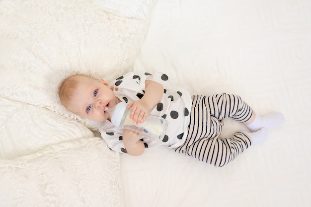 baby 8 months old lying on the bed in pajamas and drinking milk from a bottle, baby food concept