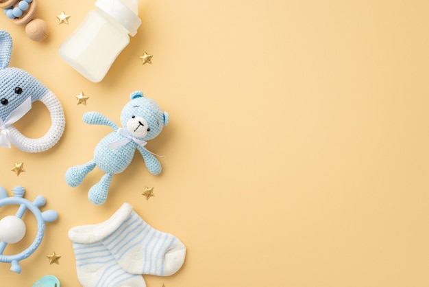 Baby accessories concept Top view photo of knitted bunny rattle toy teddybear toy blue teether milk bottle tiny socks and gold stars on isolated pastel beige background with empty space