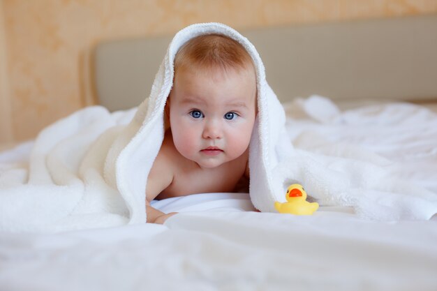 Ребенок после купания, завернутый в полотенце, лежит на кровати