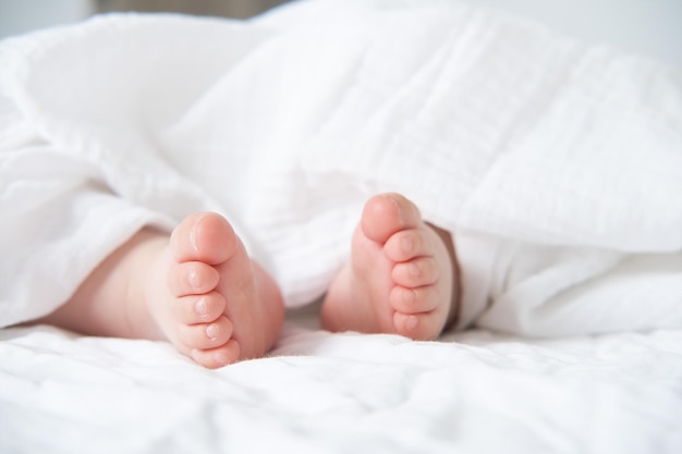 Baby bare feet on a white bed with a white blanket