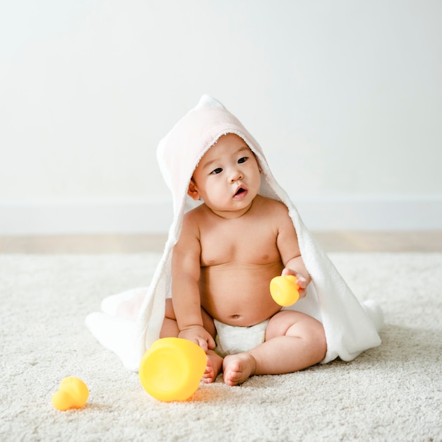 Bambino in un telo da bagno con anatre di gomma