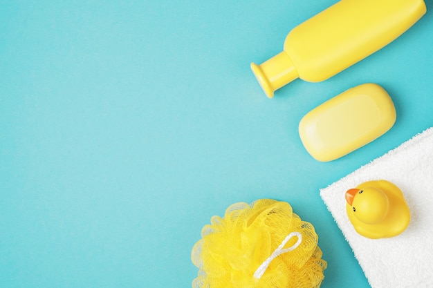 赤ちゃんの入浴アクセサリーフラットレイ。ゴム製のアヒル、シャンプー、手ぬぐい、青い背景の黄色い石鹸。上面図、コピースペース