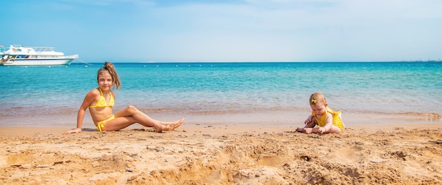 Baby and big sister on the beach near the sea