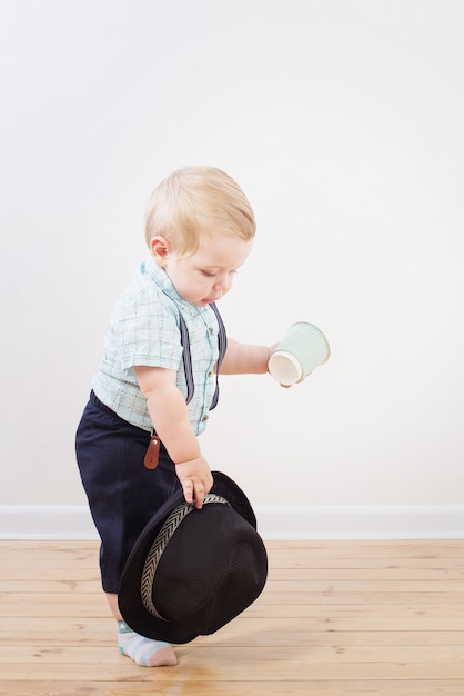 Baby in black hat, shirt and suspenders shorts  at home