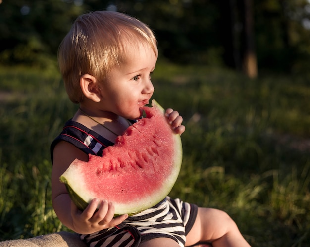 Baby blond boy eat watermelon and smile. 