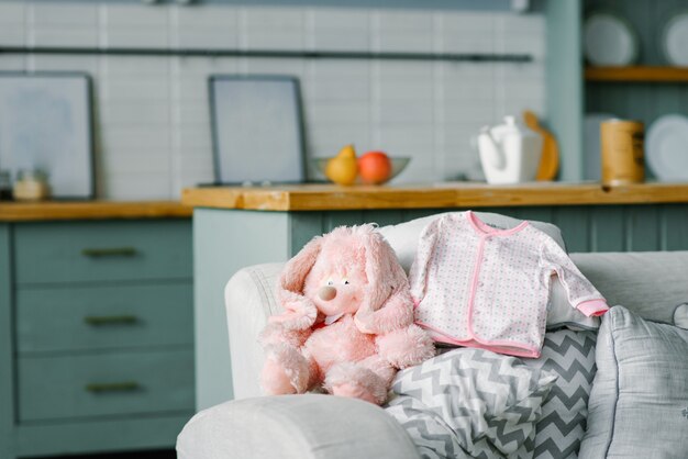 A baby blouse for a baby is lying on the sofa and a soft pink toy hare is sitting next to it. Copying space