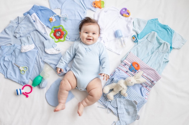 A baby in blue clothes is lying among children's accessories and clothes