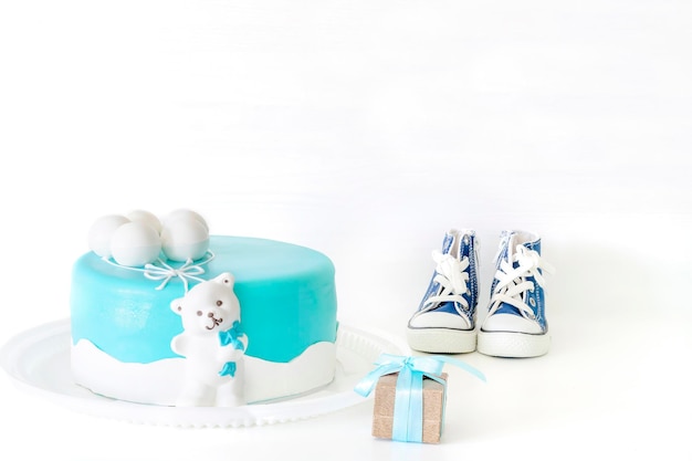 복사 공간이 있는 소년을 위한 베이비 샤워 파티를 위한 파란색으로 설정된 어린이의 첫 번째 생일 축하를 위한 숫자 하나의 촛불 선물 상자와 작은 운동화로 장식된 베이비 블루 맛있는 케이크