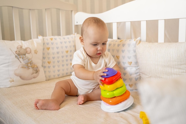 a baby in a bodysuit plays in a crib with a pyramid