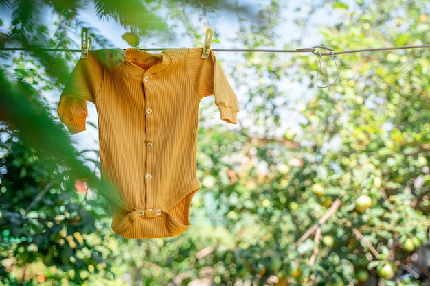 赤ちゃんのボディスーツは、夏の庭の背景に洗濯ばさみでロープにぶら下がっています。