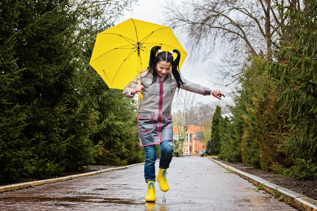 Baby boomer e salute mentale felice donna anziana in impermeabile giallo con ombrello giallo che salta