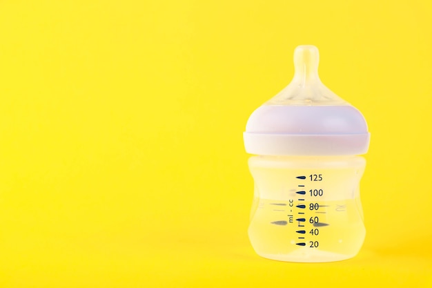 Baby bottle for milk with water and a pacifier on a yellow 