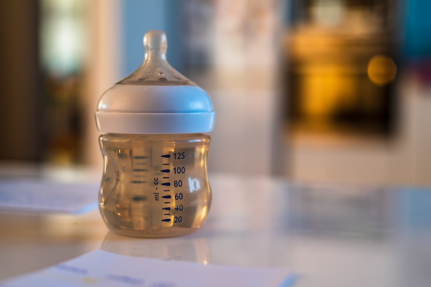 Baby bottle with nipple and water on white table