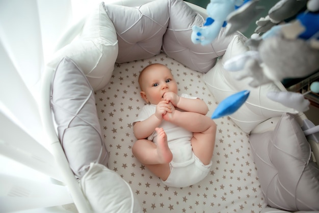 baby boy 5 months old in a white bodysuit lying in a crib top view