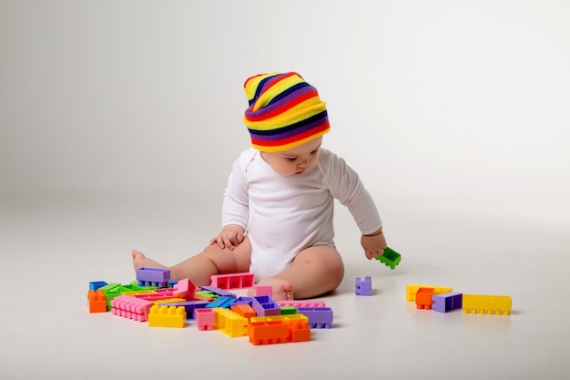 малыш 9 месяцев играет с разноцветным конструктором на белой стене