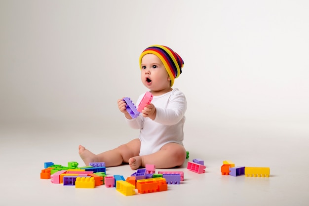 baby boy 9 months old playing with a multi-colored constructor on a white wall