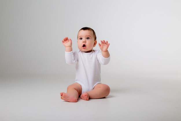 baby boy 9 months in a white bodysuit sitting on a white wall