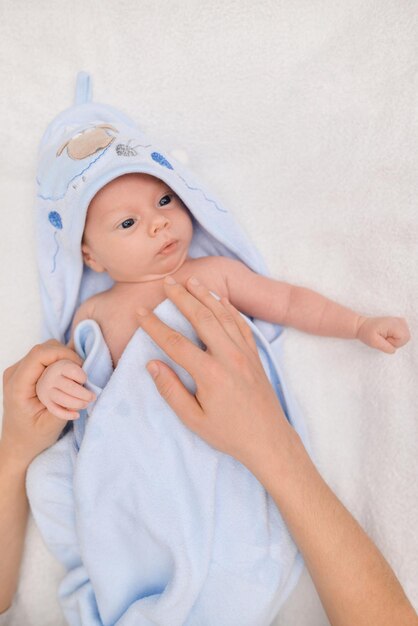 Baby boy after bath covered with blue towel and moms hands drying it