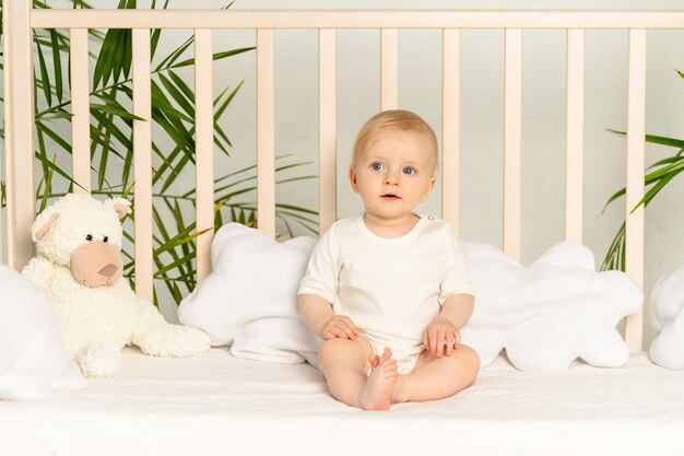 Baby boy blonde with blue eyes in a white bodysuit on a bed with cotton underwear at home before going to bed