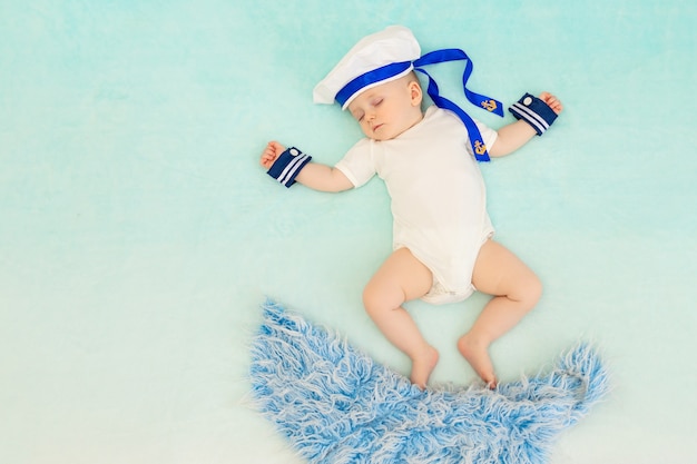 A baby boy on a blue background sleeps in a sailor suit and swims on the waves in his sleep