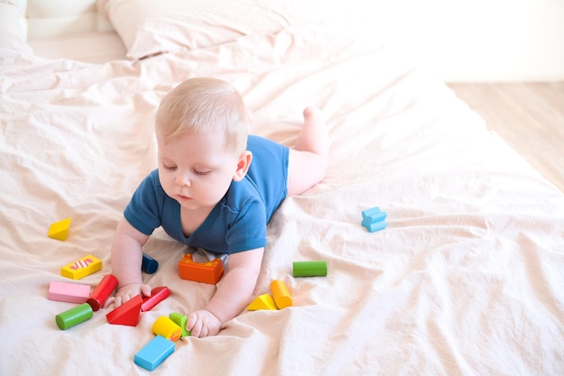 Baby boy in blue bodysuit playing with colorful wooden eco toys on bed