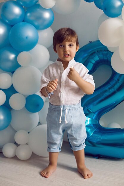Baby boy in blue pants and shirt standing on the floor in blue and white balloons
