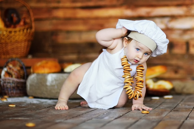 Baby boy in a chefs hat and apron with a bunch of bagels around his neck on a wooden background