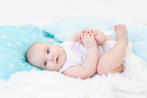 Baby boy in the crib before going to bed with blue textiles playing with his feet, cute six-month-old baby