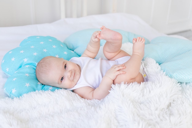 Baby boy in the crib before going to bed with blue textiles playing with his feet, cute six-month-old baby