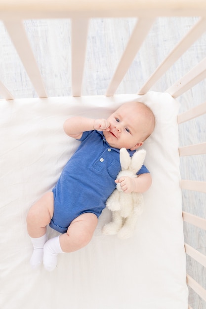 Baby boy in a crib lies on his back, a happy newborn wakes up