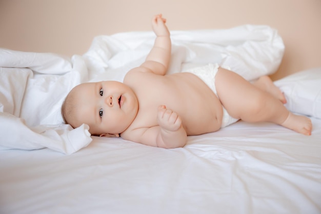 baby boy in a diaper is lying on a white sheet, covered with a blanket in the bedroom on the bed