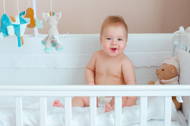 a baby boy in a diaper is sitting in a crib in the bedroom