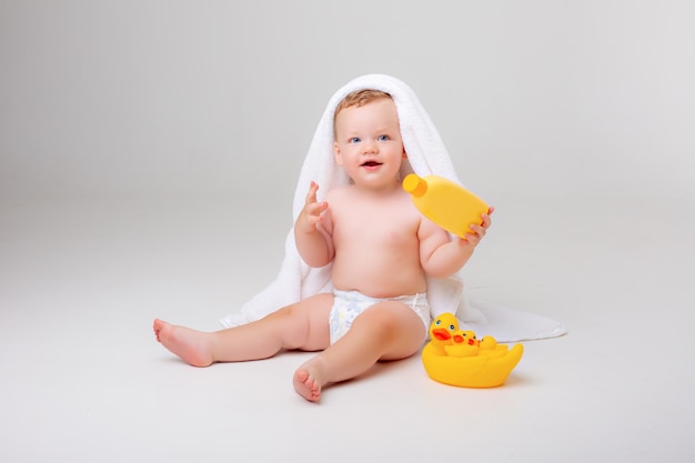 Baby boy in a diaper wrapped in a towel with toys rubber duck on a white background