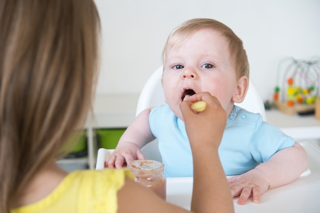 Baby boy eating bland mashed food sitting on high chair older sister feeding child