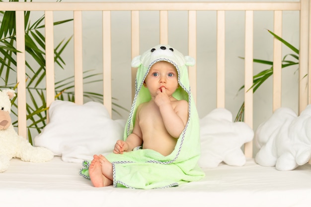 Baby boy in green towel after bath on bed at home
