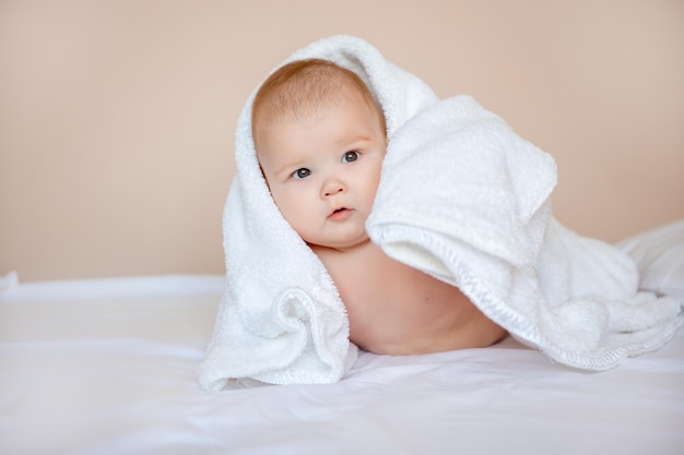 Bambino a casa in camera da letto sdraiato su un lenzuolo bianco avvolto in un asciugamano dopo il bagno