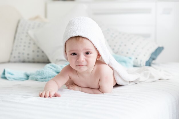 Baby boy in hooded towel crawling on bed after having bath