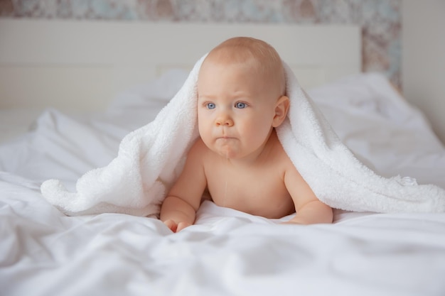 아기는 흰색 담요로 덮인 침대에서 침실에서 기어다닌다