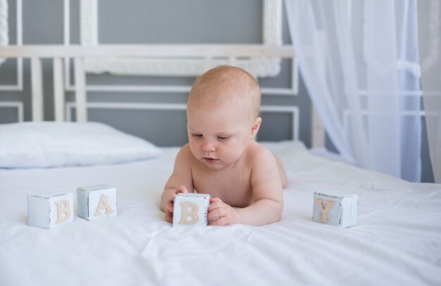 Baby boy is lying on the bed and playing with wooden cubes with the word baby