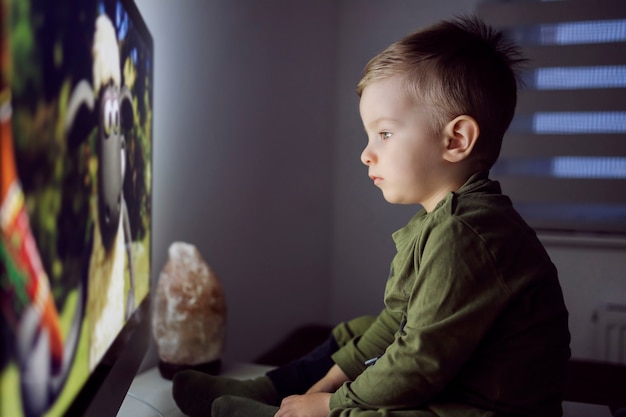 Мальчик сидит прямо перед телевизором и смотрит мультфильм