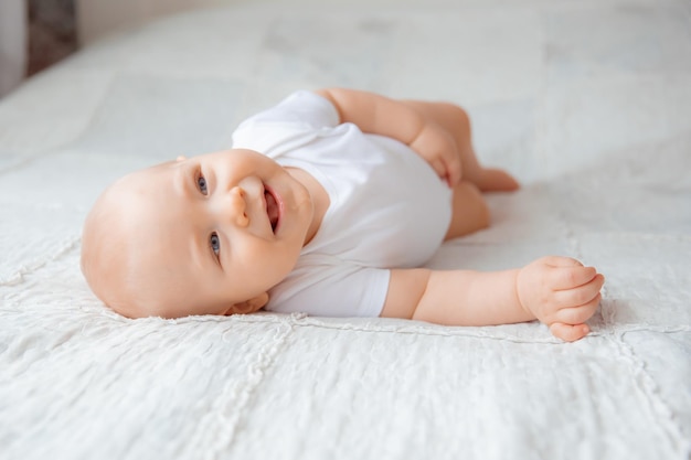 Baby boy lies in a bodysuit on a white bed in a bright bedroom turns over