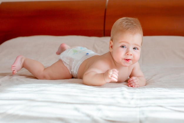 Baby boy lies in a diaper on the bed in the bedroom