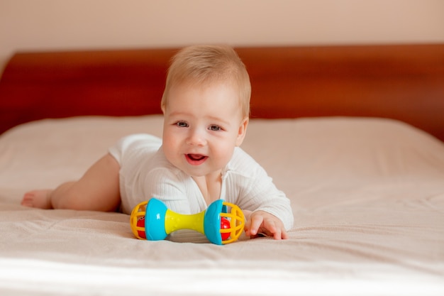 Baby boy lies on his stomach with a toy on the bed in the bedroom