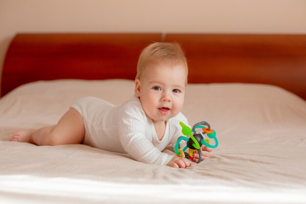 Baby boy lies on his stomach with a toy on the bed in the bedroom